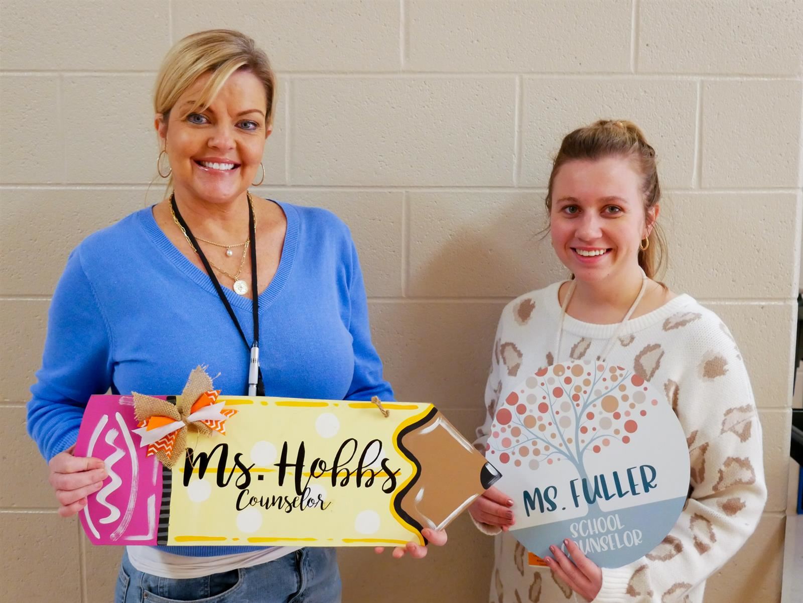 Two school counselors holding up a sign with names on them. 